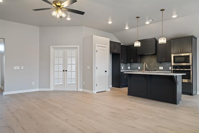 kitchen with a kitchen island with sink, backsplash, stainless steel appliances, decorative light fixtures, and vaulted ceiling