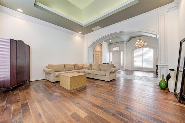 living room with a raised ceiling, dark hardwood / wood-style flooring, ornamental molding, and a notable chandelier