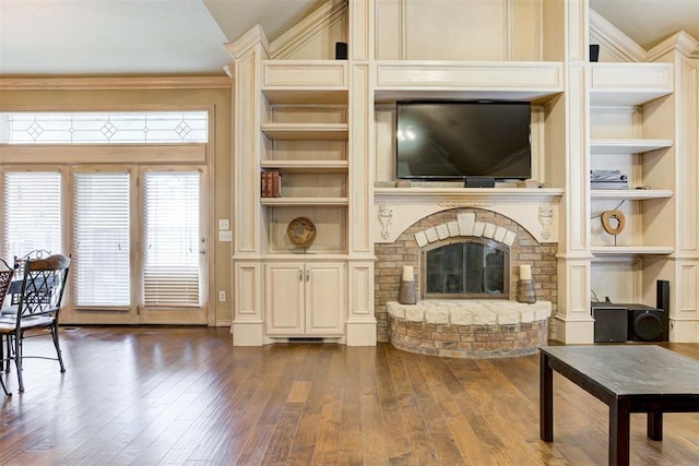 living room with built in shelves, dark hardwood / wood-style flooring, ornamental molding, and a brick fireplace