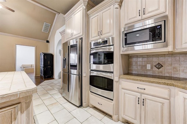 kitchen featuring lofted ceiling, ornamental molding, appliances with stainless steel finishes, tasteful backsplash, and light tile patterned flooring