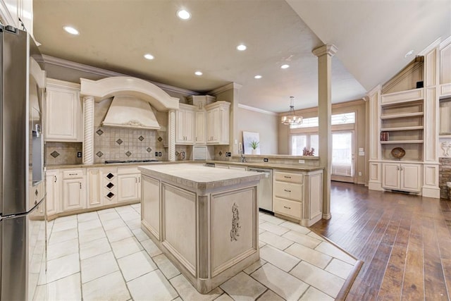 kitchen with appliances with stainless steel finishes, decorative columns, decorative light fixtures, a center island, and light hardwood / wood-style floors