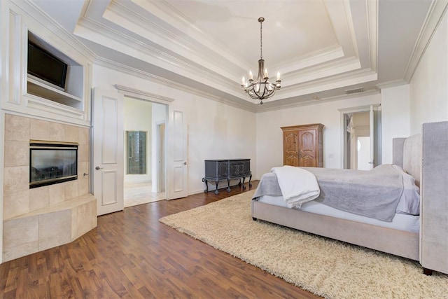 bedroom featuring a tray ceiling, crown molding, dark wood-type flooring, a tile fireplace, and an inviting chandelier