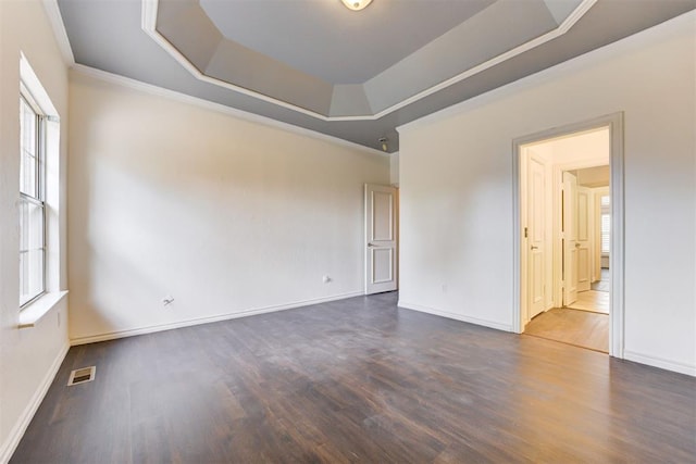 empty room with dark hardwood / wood-style floors, a raised ceiling, and crown molding