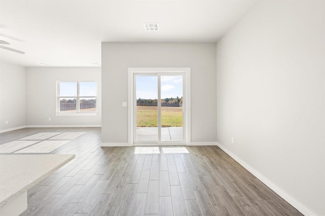 empty room featuring a wealth of natural light, ceiling fan, and light wood-type flooring