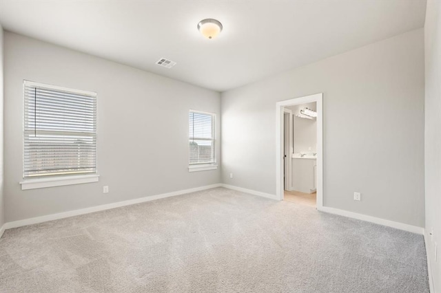 unfurnished bedroom featuring ensuite bathroom, light colored carpet, and a spacious closet