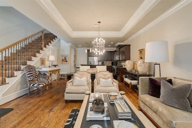 living room featuring hardwood / wood-style flooring, a chandelier, crown molding, and a tray ceiling