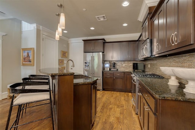 kitchen with backsplash, a center island with sink, hanging light fixtures, light wood-type flooring, and stainless steel appliances