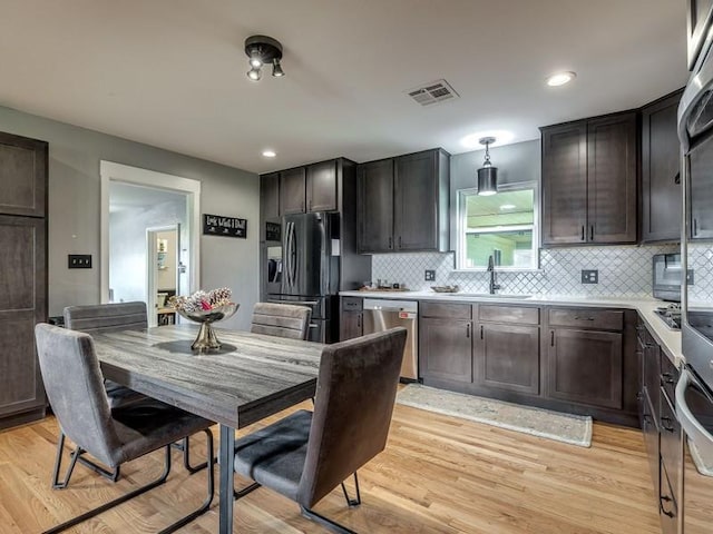 kitchen featuring backsplash, sink, hanging light fixtures, appliances with stainless steel finishes, and light hardwood / wood-style floors