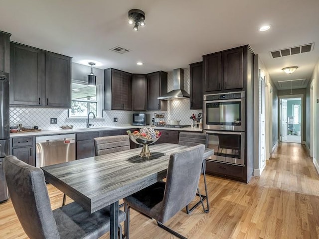 kitchen featuring tasteful backsplash, wall chimney exhaust hood, stainless steel appliances, and light hardwood / wood-style floors