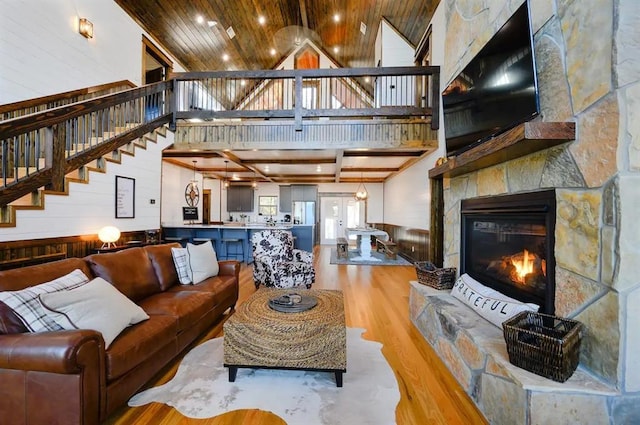 living room featuring wood walls, high vaulted ceiling, a stone fireplace, light hardwood / wood-style floors, and wood ceiling