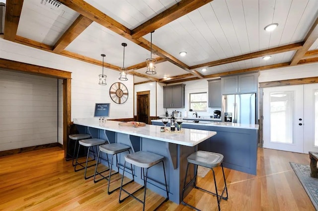 kitchen with stainless steel fridge, light wood-type flooring, beamed ceiling, gray cabinets, and hanging light fixtures