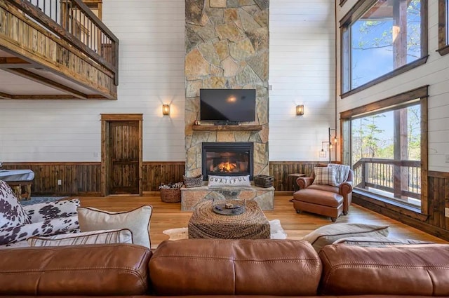 living room with a stone fireplace, wood-type flooring, a towering ceiling, and wooden walls