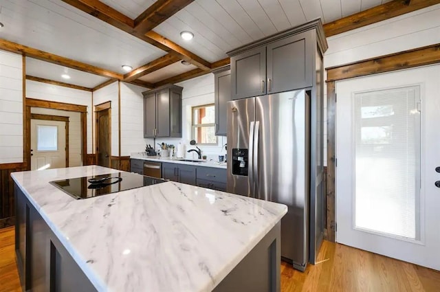 kitchen with light wood-type flooring, stainless steel fridge, a center island, and light stone counters