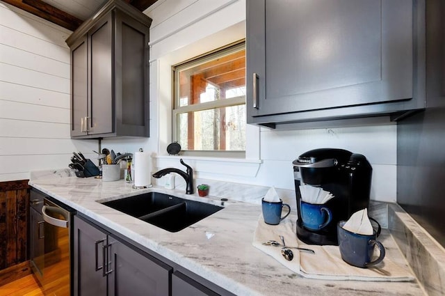 kitchen with light stone counters, stainless steel dishwasher, wood walls, and sink