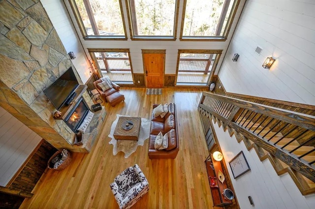 living room featuring a stone fireplace, wooden walls, a towering ceiling, and wood-type flooring