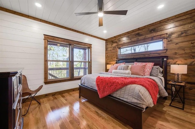 bedroom with ceiling fan, wood walls, and light wood-type flooring