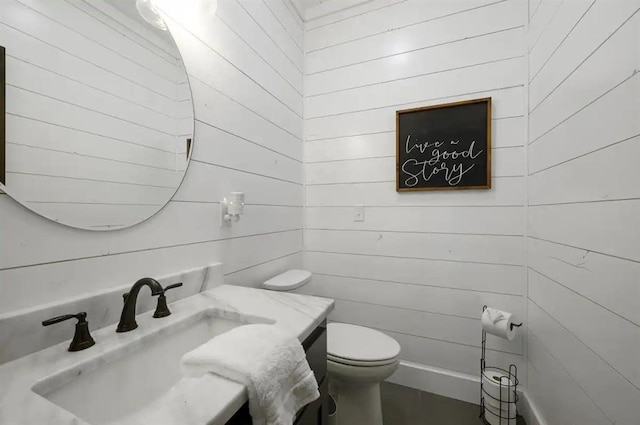 bathroom with vanity, wood walls, and toilet