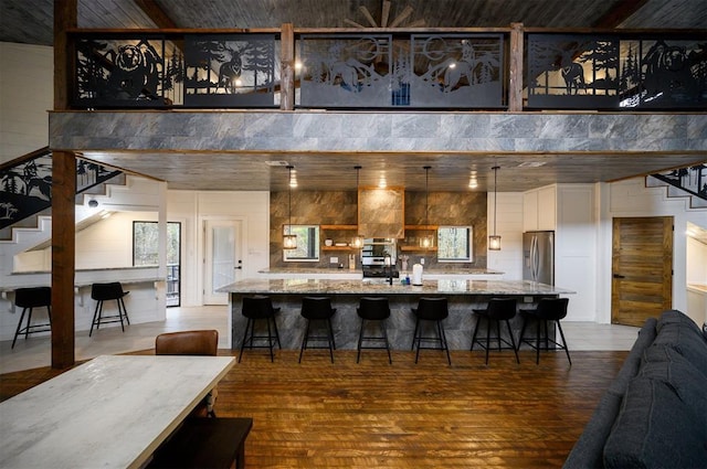 kitchen with a kitchen bar, stainless steel refrigerator with ice dispenser, light stone counters, hardwood / wood-style floors, and hanging light fixtures