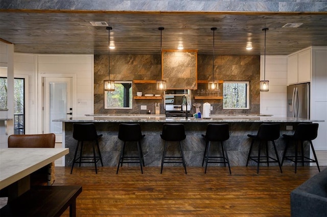 kitchen featuring a breakfast bar area, stainless steel fridge with ice dispenser, pendant lighting, and dark wood-type flooring