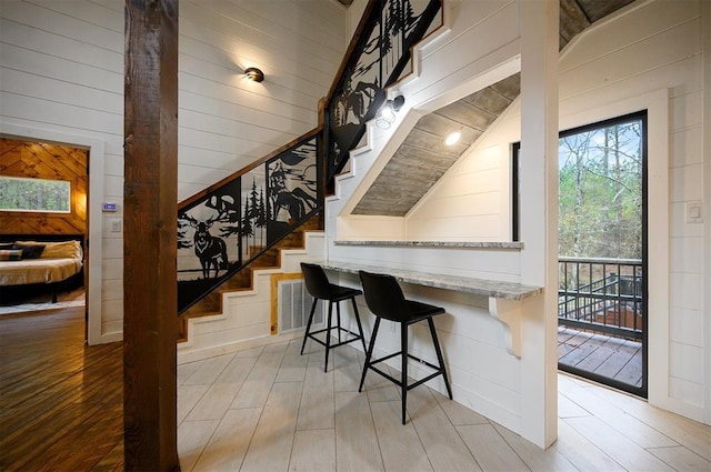 bar featuring light hardwood / wood-style floors, light stone counters, lofted ceiling, and wooden walls