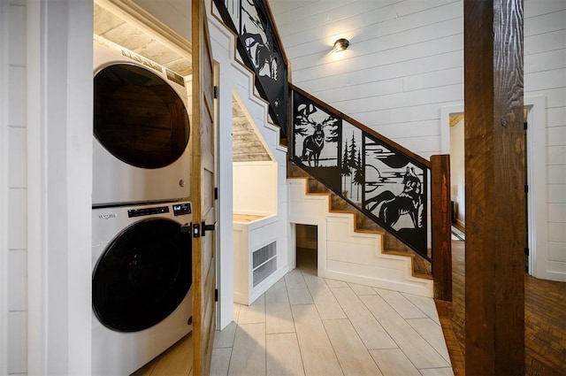 laundry area with wooden walls and stacked washing maching and dryer