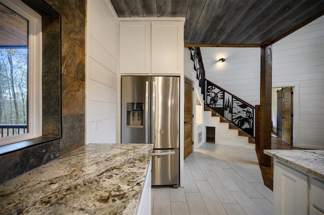 kitchen featuring stainless steel fridge with ice dispenser, wooden walls, light stone counters, and a healthy amount of sunlight