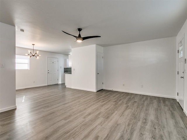 unfurnished living room featuring ceiling fan with notable chandelier and wood-type flooring