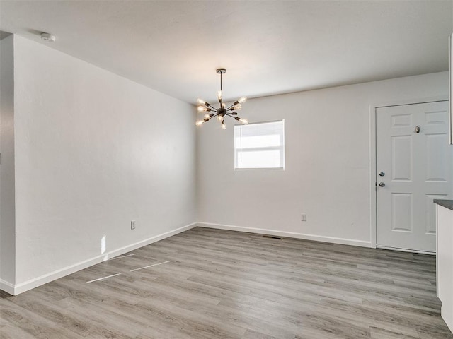 spare room featuring light wood-type flooring and an inviting chandelier