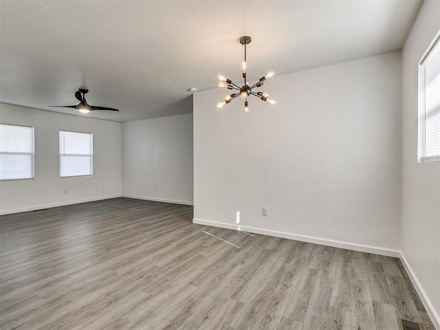 unfurnished room with ceiling fan with notable chandelier and light hardwood / wood-style flooring