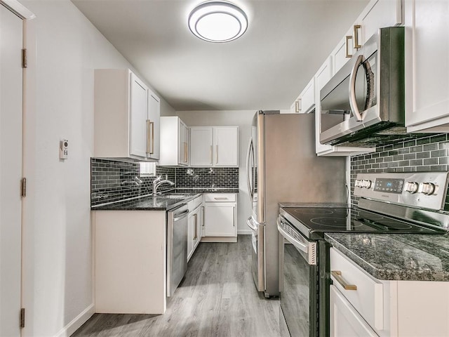 kitchen with white cabinets, dark stone countertops, light wood-type flooring, tasteful backsplash, and stainless steel appliances