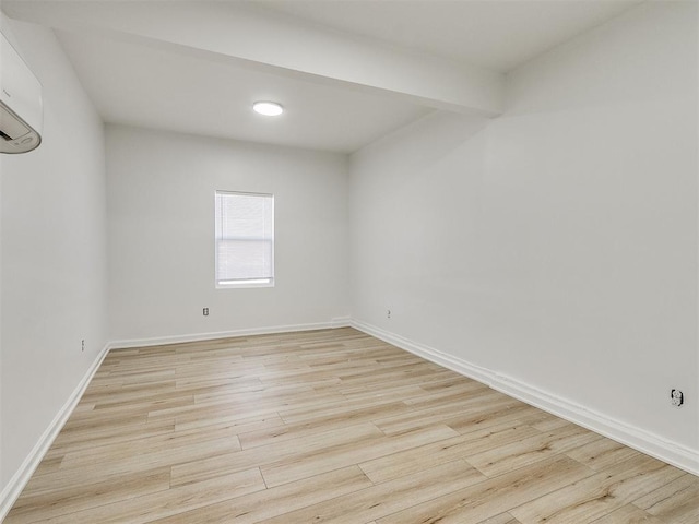 empty room with a wall unit AC, beamed ceiling, and light hardwood / wood-style floors