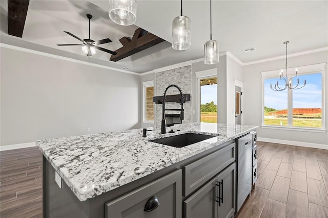 kitchen with light stone countertops, stainless steel dishwasher, ceiling fan with notable chandelier, sink, and an island with sink