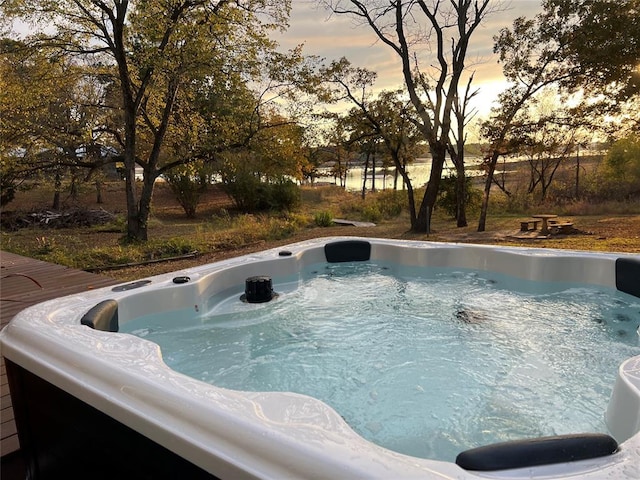 pool at dusk featuring a hot tub