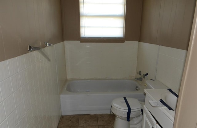 bathroom with tile patterned flooring, toilet, a bathtub, vanity, and tile walls