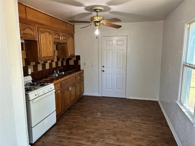 kitchen featuring dark wood-style flooring, brown cabinets, tasteful backsplash, a sink, and white gas range oven