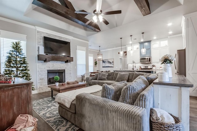 living room with ceiling fan, a stone fireplace, beamed ceiling, dark hardwood / wood-style floors, and ornamental molding