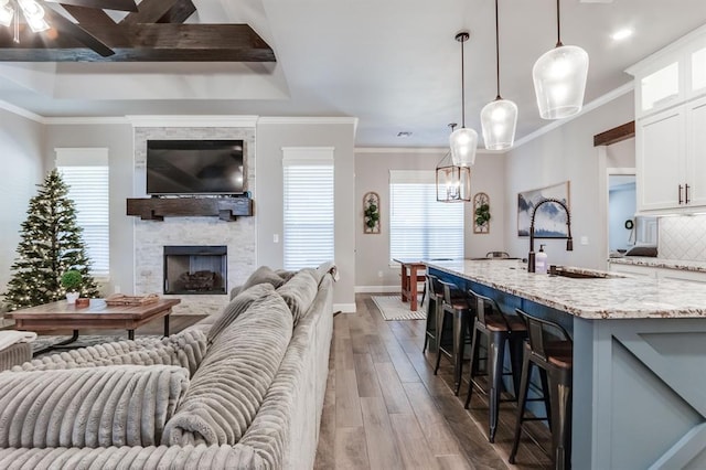 living room featuring ornamental molding, ceiling fan, sink, light hardwood / wood-style flooring, and a fireplace