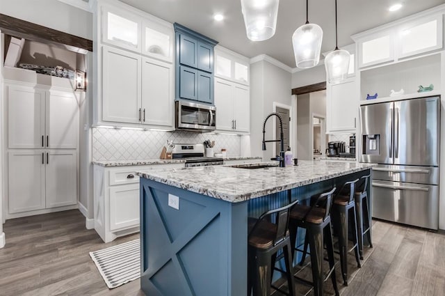 kitchen with stainless steel appliances, hardwood / wood-style floors, an island with sink, decorative light fixtures, and white cabinets