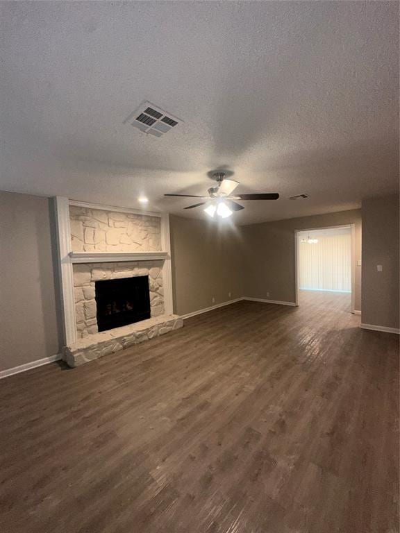 unfurnished living room featuring a stone fireplace, ceiling fan, dark hardwood / wood-style floors, and a textured ceiling