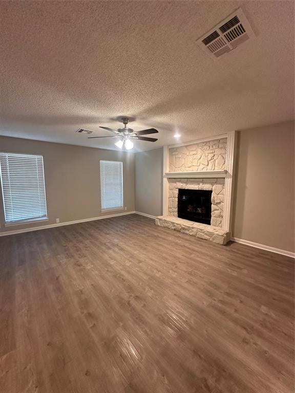 unfurnished living room featuring a fireplace, ceiling fan, wood-type flooring, and a textured ceiling