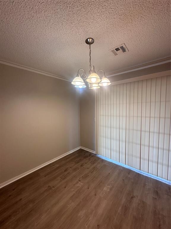 spare room featuring dark hardwood / wood-style flooring, a chandelier, a textured ceiling, and ornamental molding