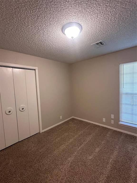 unfurnished bedroom with multiple windows, a closet, carpet, and a textured ceiling