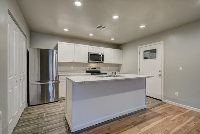 kitchen featuring white cabinets, light hardwood / wood-style floors, an island with sink, and appliances with stainless steel finishes