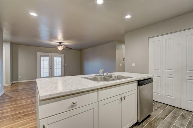 kitchen featuring sink, stainless steel dishwasher, light wood-type flooring, an island with sink, and white cabinetry