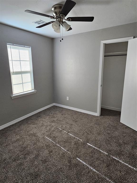 unfurnished bedroom with ceiling fan, a closet, and dark colored carpet