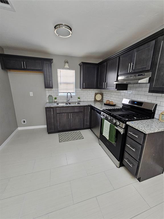 kitchen with backsplash, stainless steel appliances, light stone counters, and sink