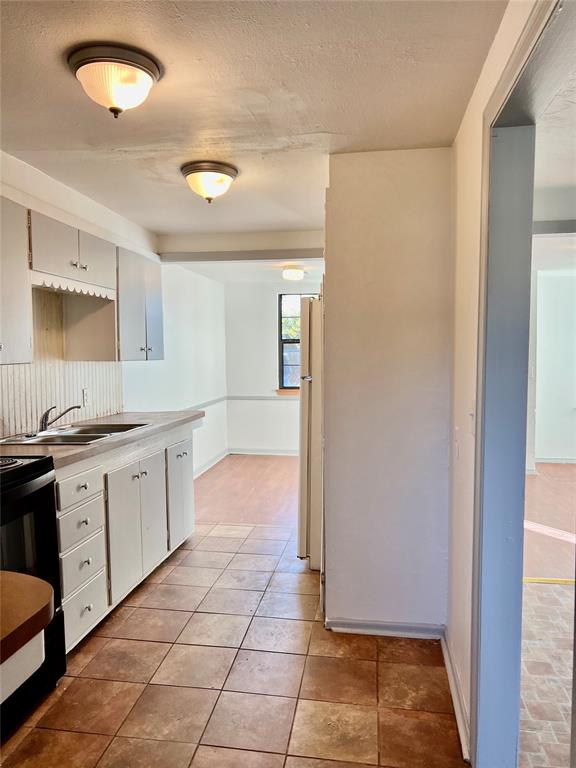 kitchen with white refrigerator, sink, a textured ceiling, electric range oven, and white cabinetry