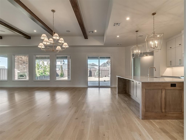 kitchen featuring a large island with sink, a notable chandelier, pendant lighting, and white cabinets