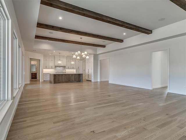 unfurnished living room with beamed ceiling, a notable chandelier, and light hardwood / wood-style flooring