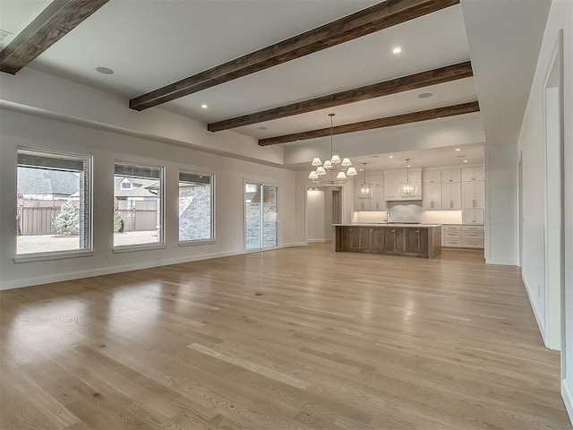 unfurnished living room featuring beam ceiling, a healthy amount of sunlight, an inviting chandelier, and light wood-type flooring